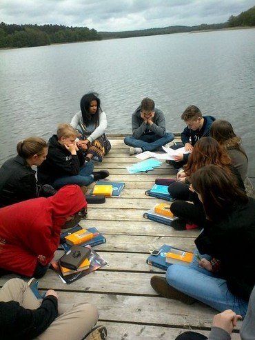Jugendliche sitzen auf einem Steg am See und lernen.